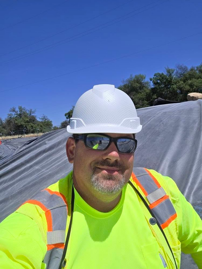Terry Weigner wearing a white hard hat and high-visibility jacket on a pond construction site.